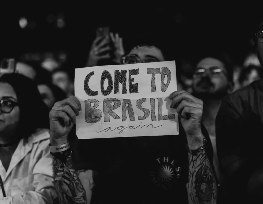 fã segurando cartaz que diz "come to Brasil again" que, em tradução direta signidica "venham novamente ao Brasil"
