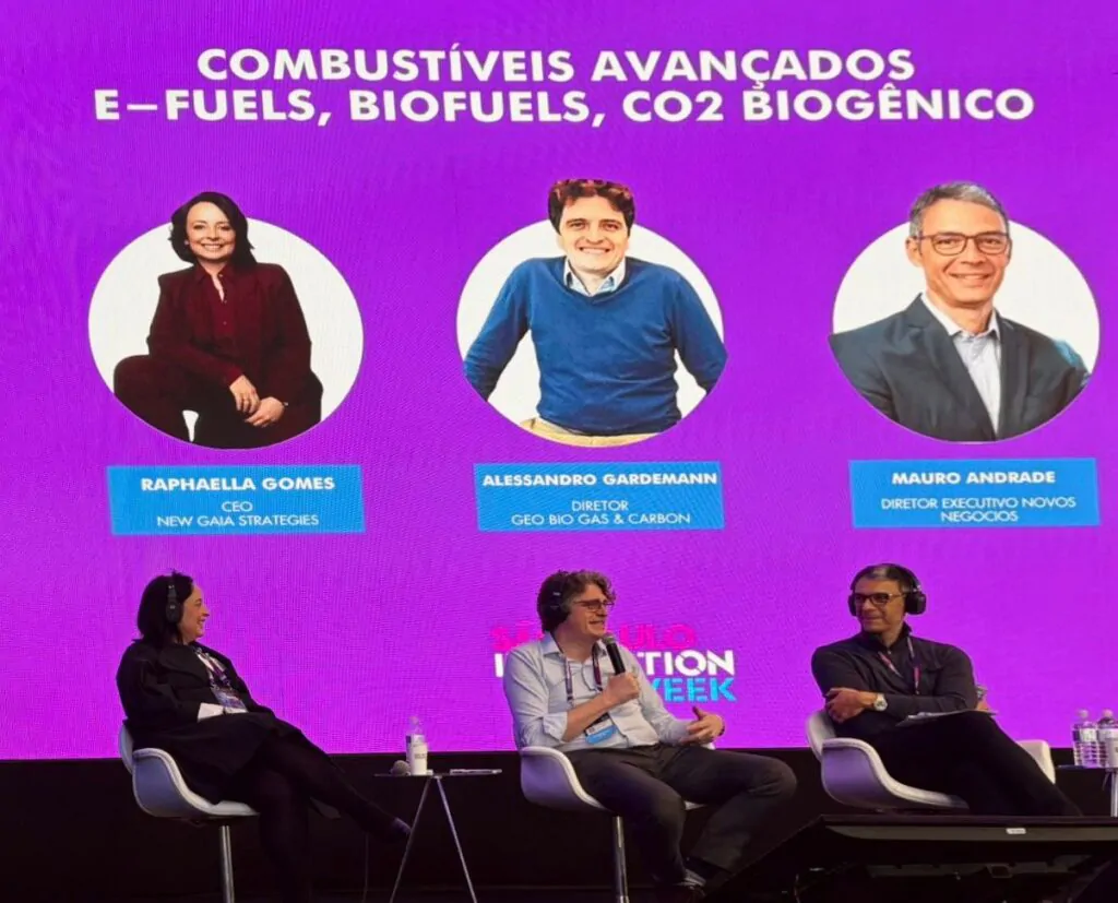 Foto mostra três pessoas em palco falando sobre transição energética.