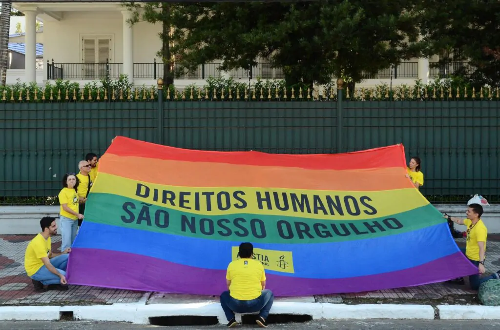 Pessoas segurando a bandeira LGBTQIA+ com os dizeres "Direitos humanos são nosso orgulho"