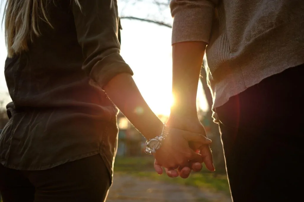 Um casal é mostrado de mãos dadas durante o entardecer, o foco é apenas em suas mãos