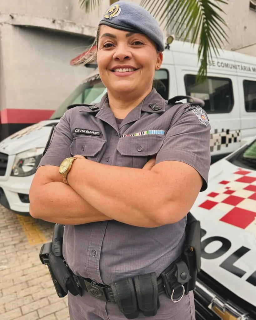 Mulher de farda policial branca sorrindo de braços cruzados